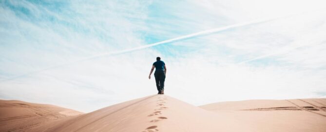 a man walking up a sand dune