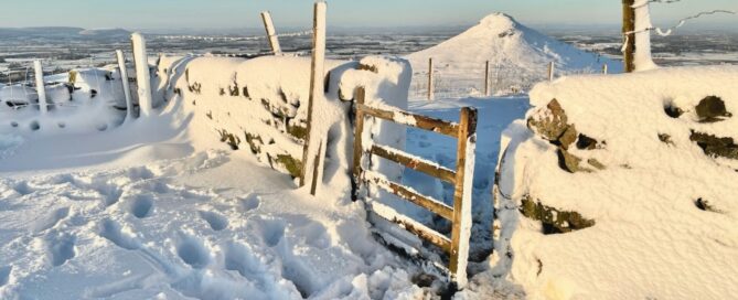 a snowy fence with a hill in the background