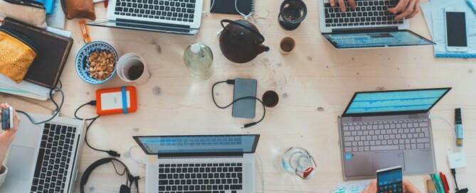 a group of people sitting around a table with laptops